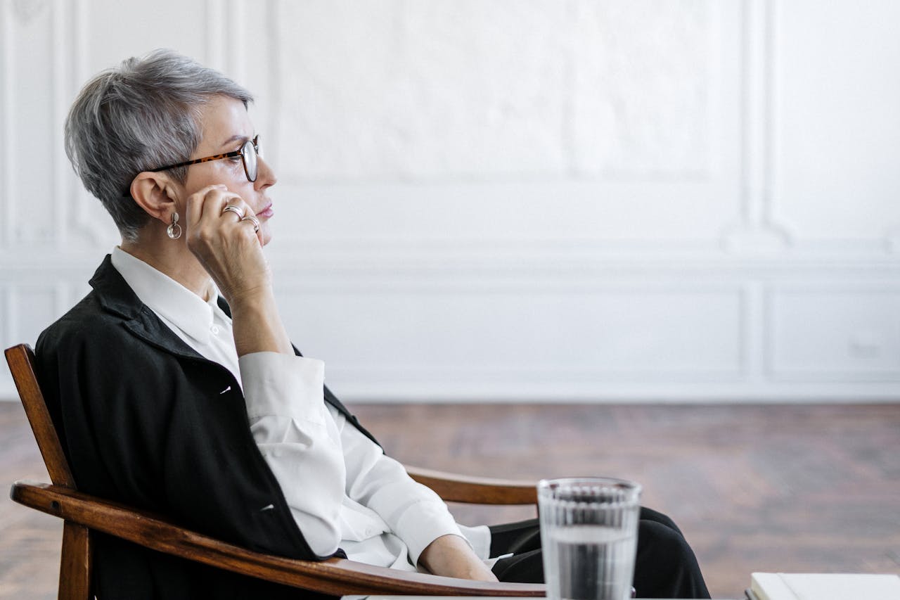 Senior woman in glasses reflecting thoughtfully in an elegant office setting.